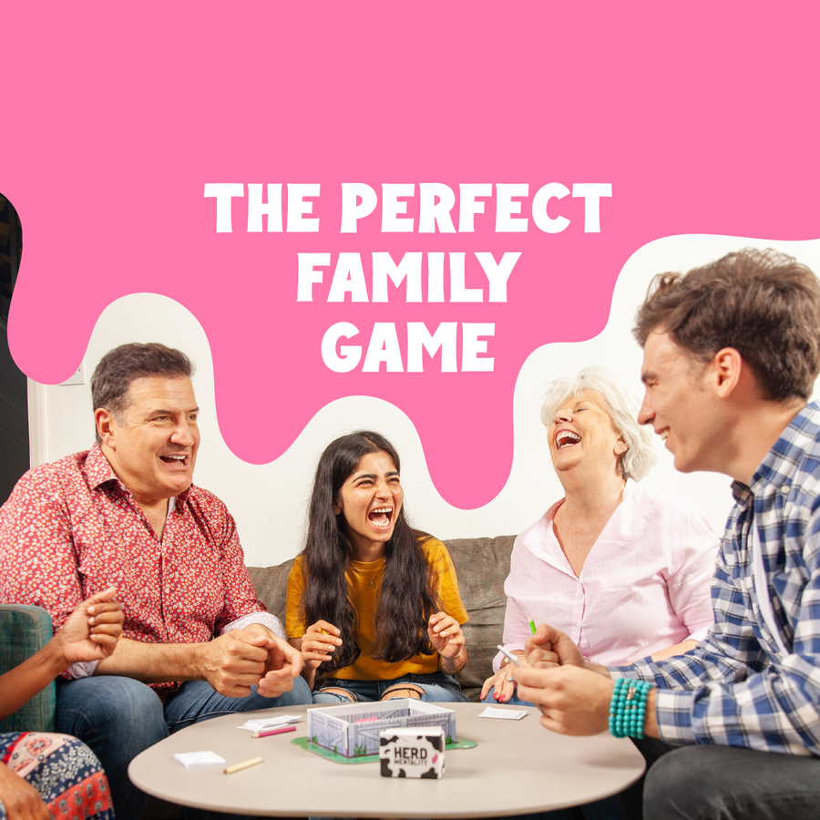 A family board game scene with four people laughing around a small table in a living room. A large pink graphic overlay at the top reads 'THE PERFECT FAMILY GAME' in white text.
