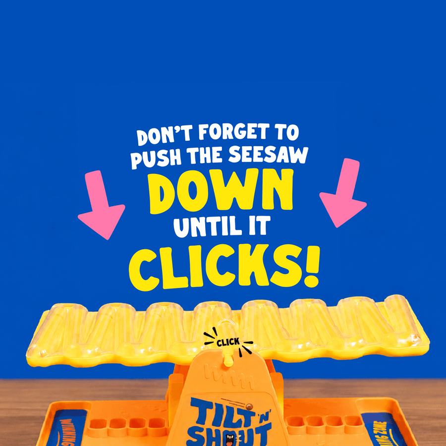 Tilt n Shout seesaw on a wooden surface, with large overlaid text reading 'DON'T FORGET TO PUSH THE SEESAW DOWN UNTIL IT CLICKS!' and pink arrows pointing down.